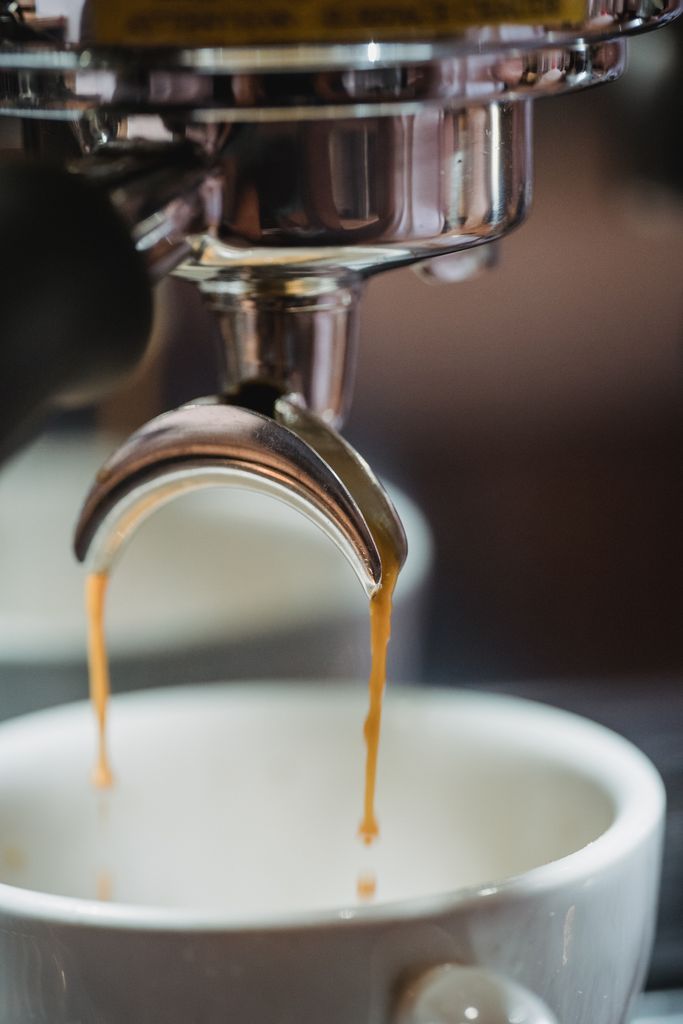 Close-up of coffee dripping into a white cup from a coffee machine for a rich espresso shot.